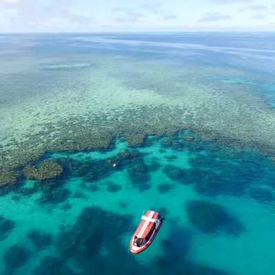 Aerial view of a red boat on clear turquoise ocean near a coral reef.
